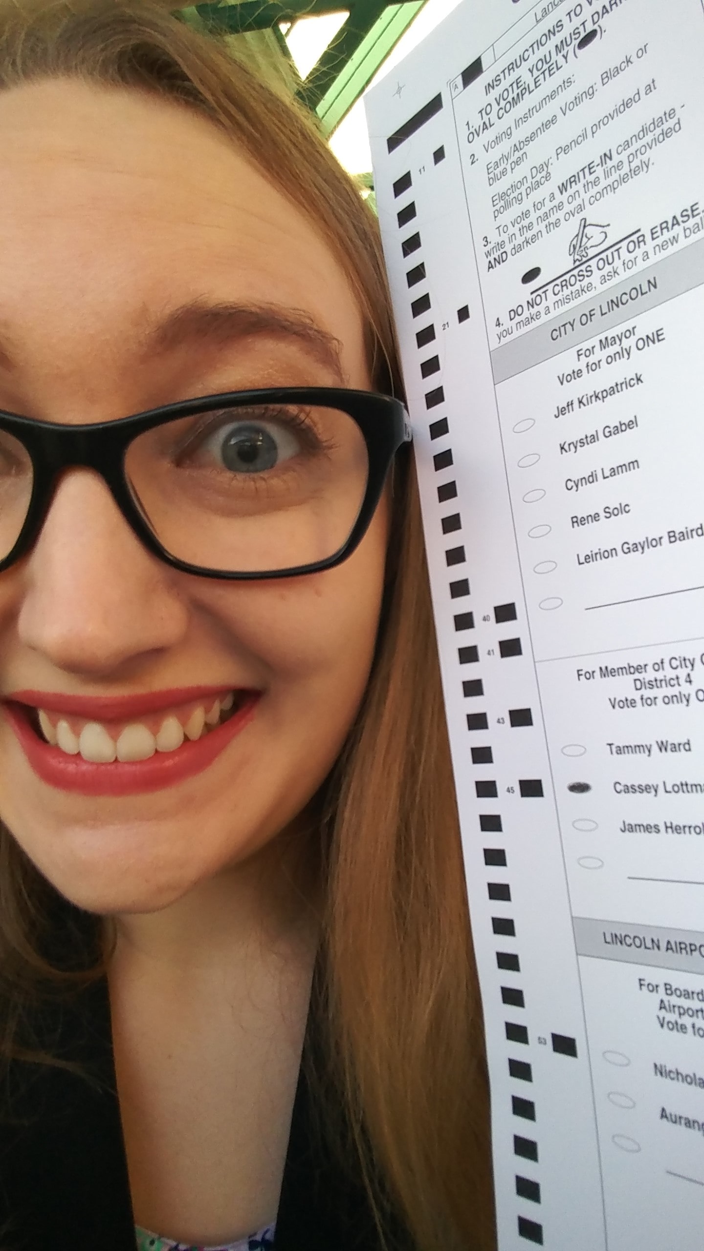 A close-up of Cassey's very excited face. She's holding a ballot with her own name on it, with the bubble filled in.